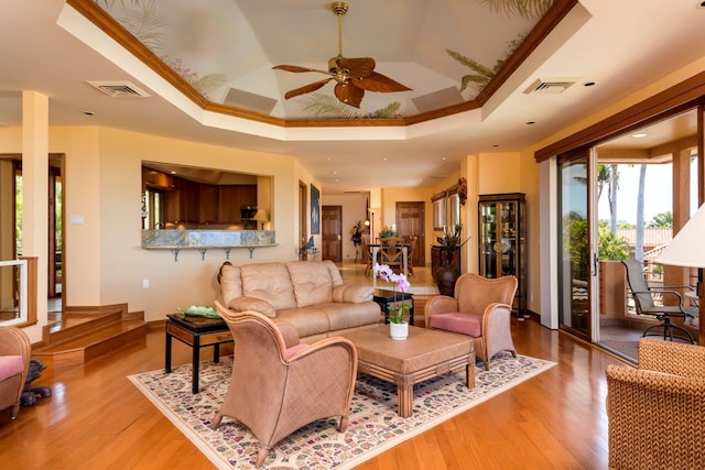 living room featuring ceiling fan, ornamental molding, a tray ceiling, and hardwood / wood-style floors