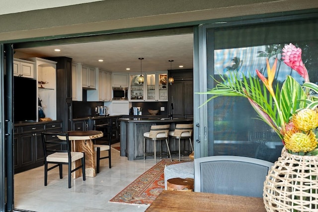 12 S Kihei Rd Unit E2, Kihei, HI 96753 - kitchen with stainless steel microwave, a kitchen breakfast bar, dark countertops, glass insert cabinets, and hanging light fixtures