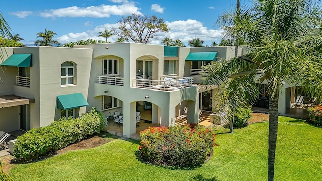 rear view of property with a yard, a balcony, and a patio