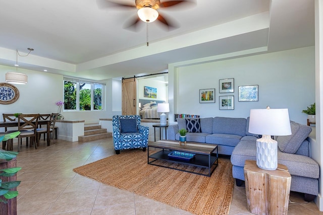 tiled living room featuring ceiling fan, a barn door, and a tray ceiling