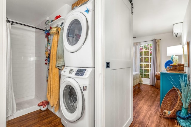 clothes washing area with hardwood / wood-style flooring, a barn door, an AC wall unit, and stacked washer / dryer