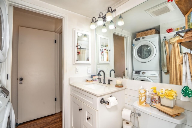 bathroom with hardwood / wood-style floors, stacked washer / drying machine, toilet, and vanity