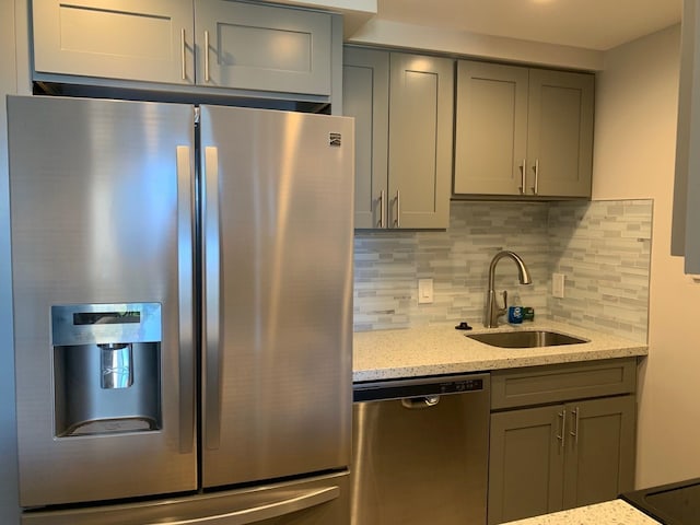 kitchen featuring light stone countertops, appliances with stainless steel finishes, backsplash, sink, and gray cabinets