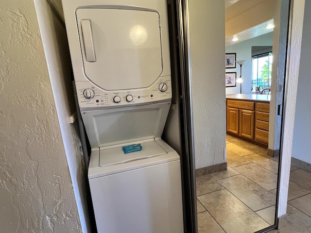 laundry room featuring baseboards, light tile patterned floors, laundry area, stacked washer and clothes dryer, and a textured wall