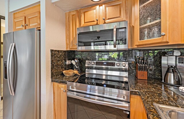 kitchen featuring stainless steel appliances, dark stone countertops, backsplash, and ceiling fan