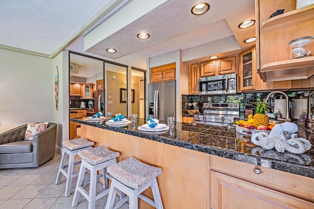 kitchen featuring light tile patterned floors, stainless steel appliances, tasteful backsplash, a kitchen bar, and kitchen peninsula