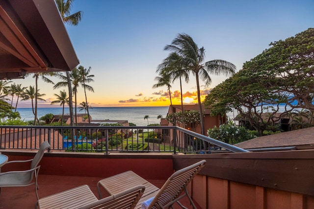 balcony at dusk featuring a water view