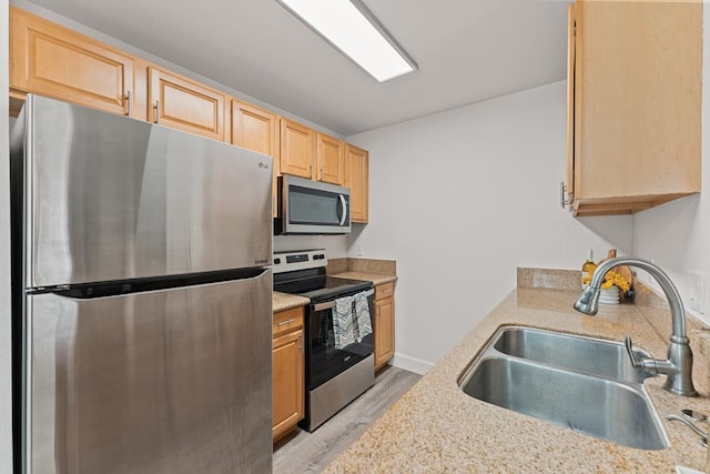 kitchen with sink, light hardwood / wood-style flooring, appliances with stainless steel finishes, light stone countertops, and light brown cabinetry