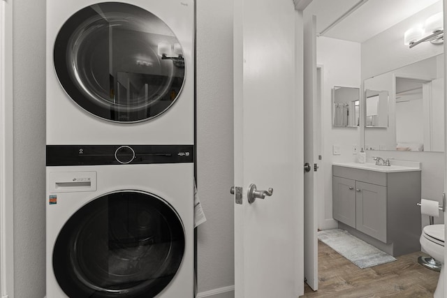 clothes washing area with light hardwood / wood-style floors, stacked washer / dryer, and sink