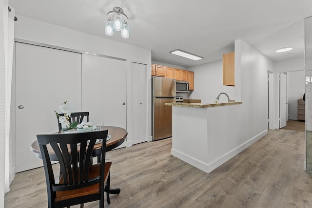 kitchen with kitchen peninsula, light hardwood / wood-style floors, light brown cabinets, and appliances with stainless steel finishes