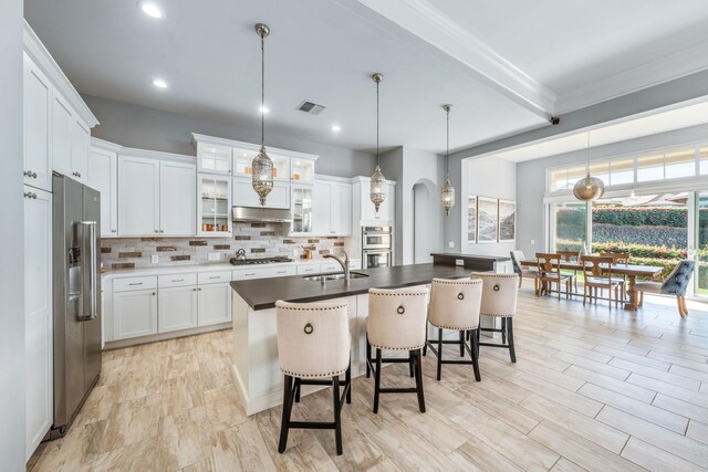 kitchen with a breakfast bar, decorative light fixtures, white cabinetry, and an island with sink