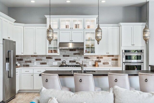 kitchen featuring white cabinetry, backsplash, stainless steel appliances, hanging light fixtures, and a kitchen breakfast bar