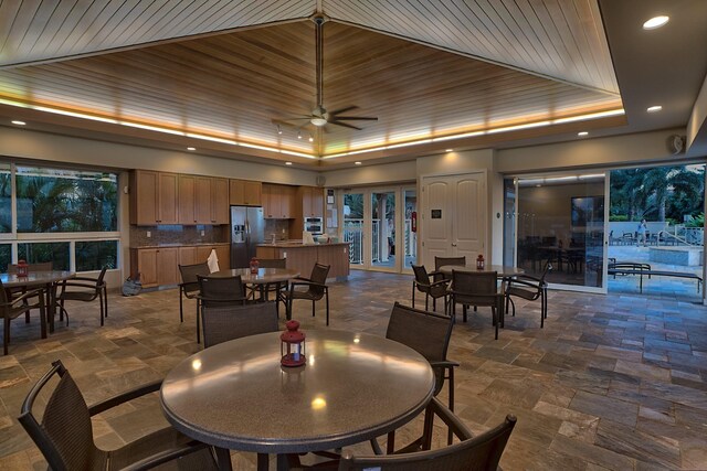 dining space featuring dark tile patterned flooring, ceiling fan, and a raised ceiling