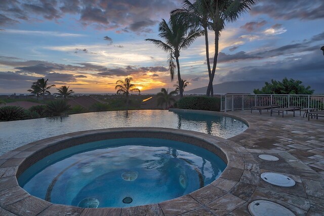 pool at dusk with an in ground hot tub and a patio