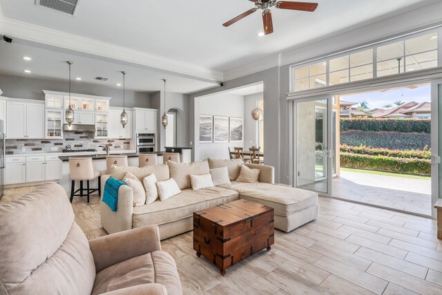 living room with ceiling fan, light hardwood / wood-style floors, ornamental molding, and plenty of natural light