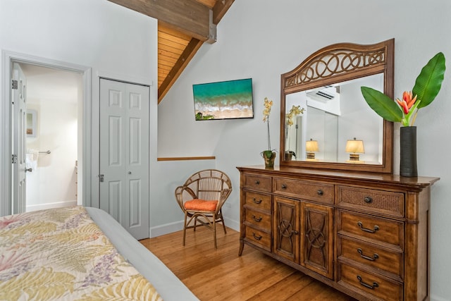 bedroom featuring a wall mounted air conditioner, light wood-type flooring, wood ceiling, vaulted ceiling with beams, and a closet