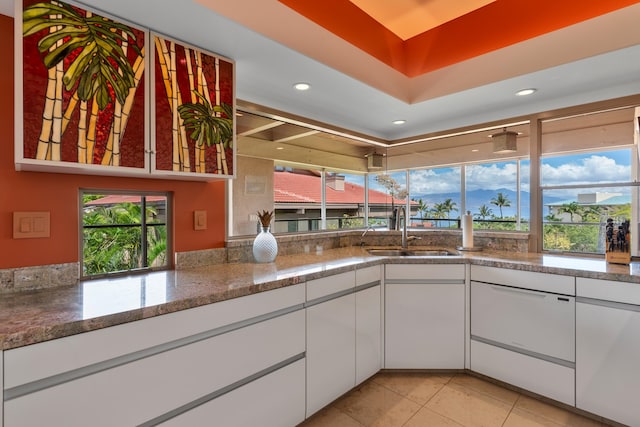 kitchen featuring light tile floors, dark stone counters, white cabinets, and sink