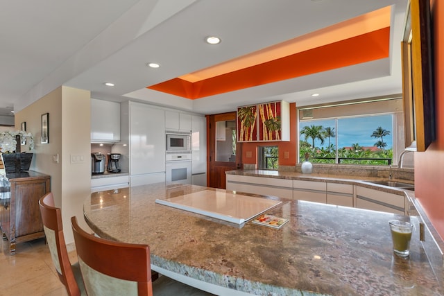 kitchen featuring stainless steel microwave, a tray ceiling, oven, white cabinetry, and sink