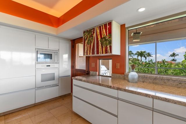 kitchen with white cabinets, stone counters, white appliances, and light tile floors