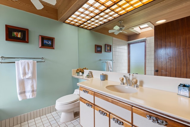 bathroom featuring tile flooring, a skylight, ceiling fan, vanity with extensive cabinet space, and toilet