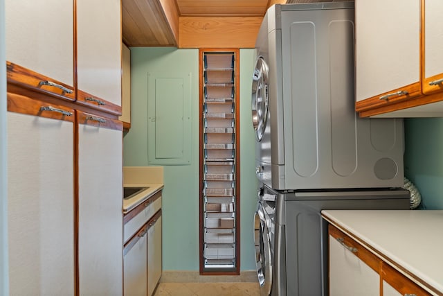 clothes washing area featuring stacked washer / dryer, cabinets, and light tile floors