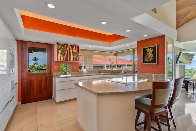 kitchen featuring a wealth of natural light, white cabinetry, light tile floors, and a kitchen bar