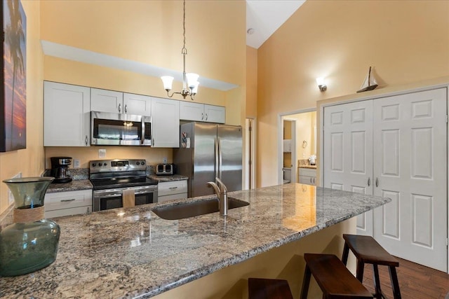 kitchen with a breakfast bar, sink, white cabinets, hanging light fixtures, and stainless steel appliances