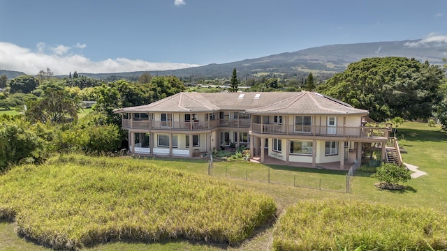 back of house with a lawn, a mountain view, and a balcony