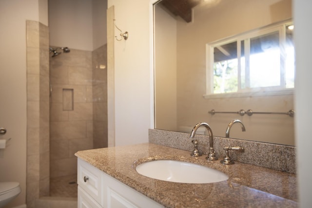 bathroom featuring a tile shower, vanity, and toilet