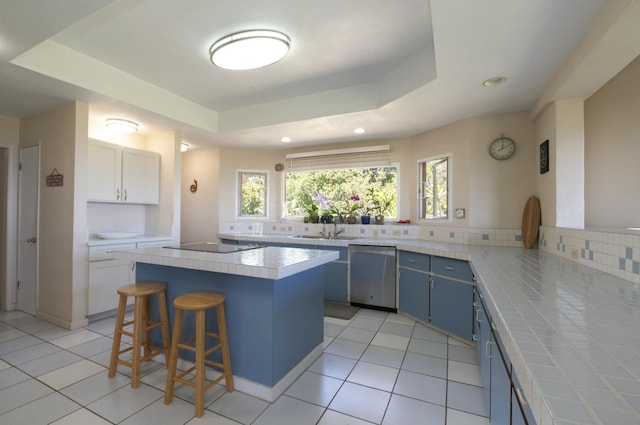 kitchen with stainless steel dishwasher, a kitchen island, a raised ceiling, and blue cabinets