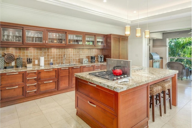 kitchen featuring a kitchen island, stainless steel gas stovetop, sink, backsplash, and hanging light fixtures