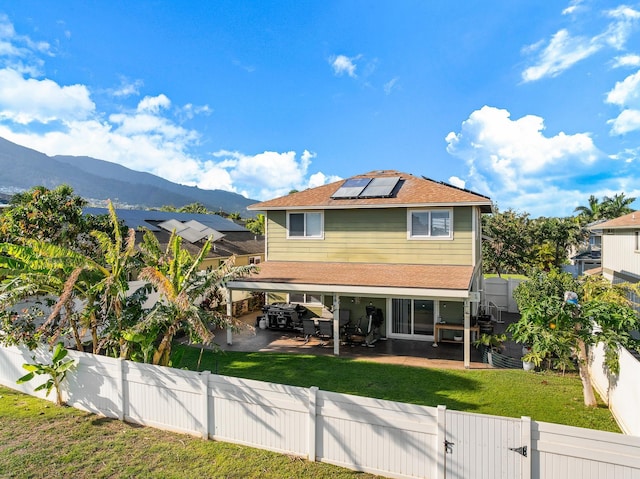 rear view of property with a patio, a gate, a fenced backyard, a mountain view, and roof mounted solar panels