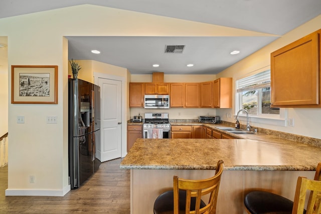 kitchen featuring visible vents, appliances with stainless steel finishes, a peninsula, wood finished floors, and a sink