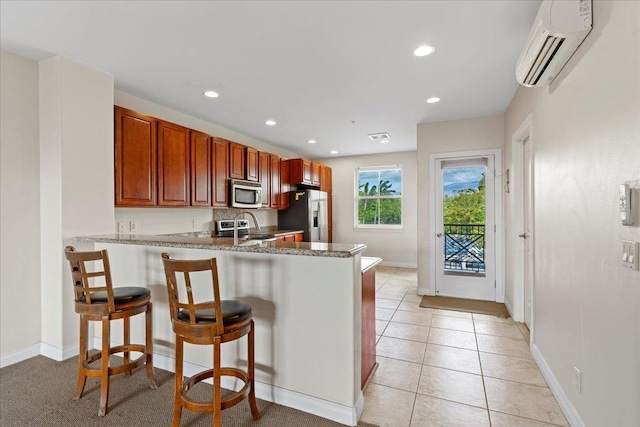 kitchen featuring appliances with stainless steel finishes, a kitchen bar, kitchen peninsula, a wall unit AC, and stone counters