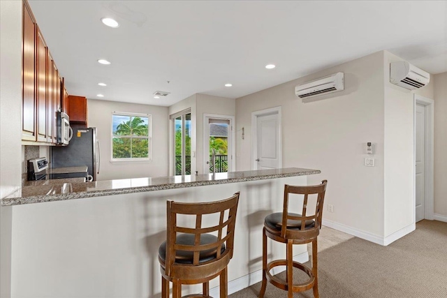 kitchen featuring kitchen peninsula, light colored carpet, an AC wall unit, and appliances with stainless steel finishes