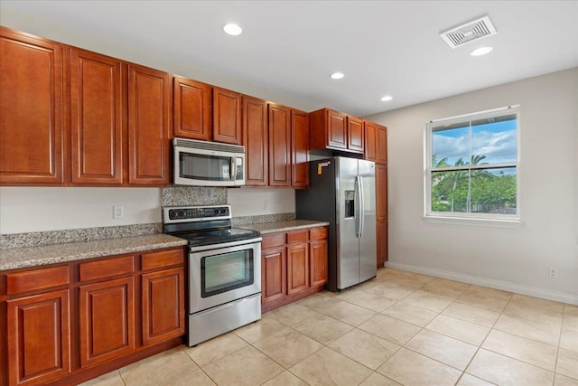 kitchen with light stone counters, light tile patterned floors, stainless steel appliances, and tasteful backsplash