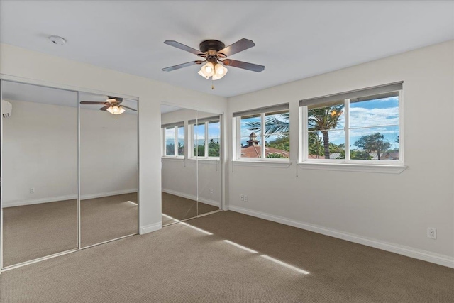 unfurnished bedroom featuring dark carpet, two closets, and ceiling fan