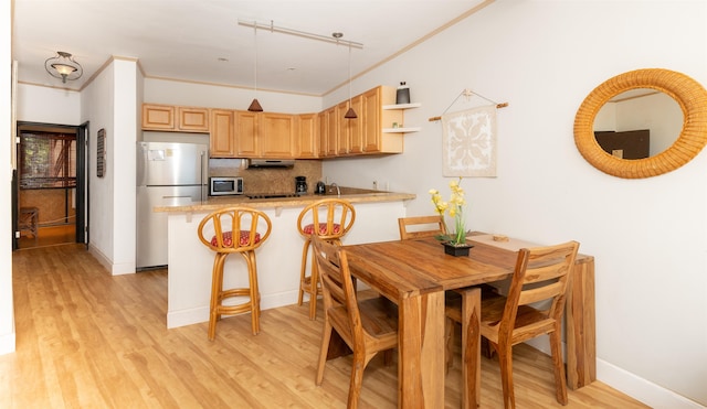 kitchen with kitchen peninsula, light brown cabinets, appliances with stainless steel finishes, a breakfast bar, and light wood-type flooring