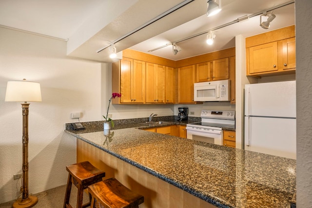 kitchen featuring white appliances, sink, dark stone countertops, kitchen peninsula, and a breakfast bar area