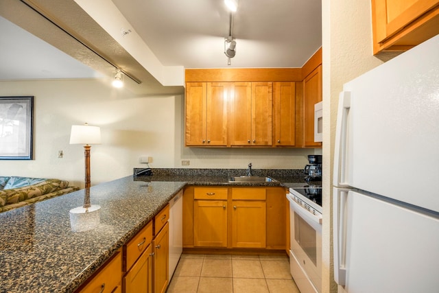 kitchen featuring track lighting, dark stone counters, white appliances, sink, and light tile patterned flooring