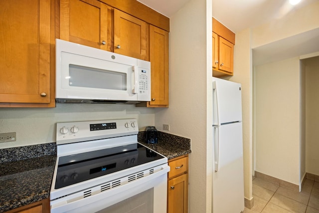 kitchen with light tile patterned floors, white appliances, and dark stone counters