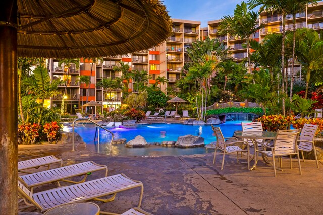 pool at dusk with pool water feature and a patio area