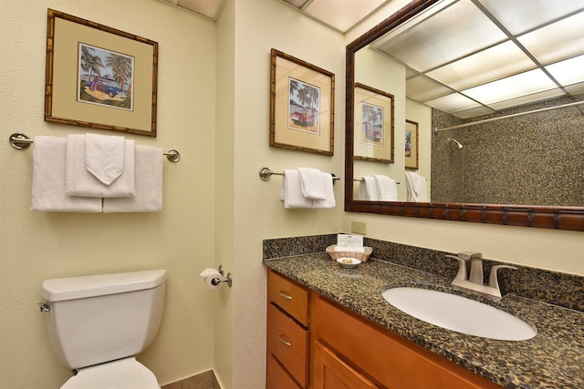 bathroom with walk in shower, a drop ceiling, vanity, and toilet