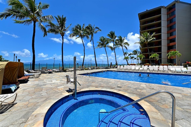 view of pool with a patio area, a water view, and a hot tub