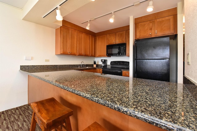 kitchen with a breakfast bar, dark stone counters, track lighting, black appliances, and kitchen peninsula