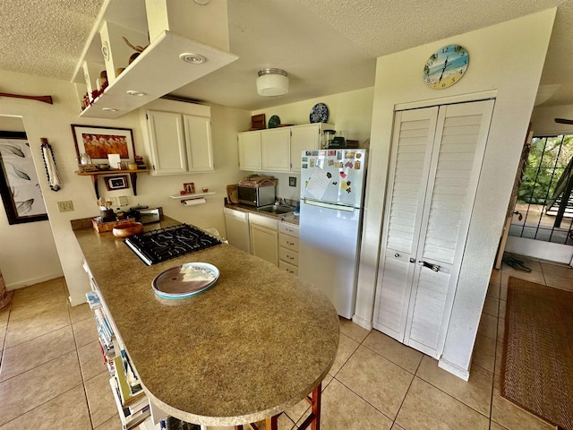 kitchen featuring black gas stovetop, a textured ceiling, white fridge, and light tile patterned floors