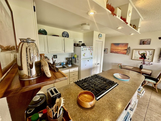 kitchen with sink, gas stovetop, a textured ceiling, light tile patterned floors, and white fridge