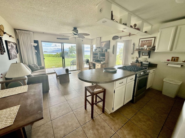 kitchen with a kitchen breakfast bar, light tile patterned floors, kitchen peninsula, stainless steel gas range oven, and a textured ceiling