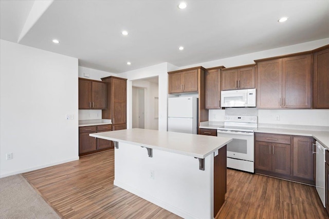 kitchen featuring white appliances, dark wood-type flooring, a breakfast bar area, light countertops, and a kitchen island