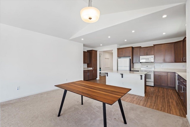 kitchen with lofted ceiling, white appliances, light countertops, and a center island